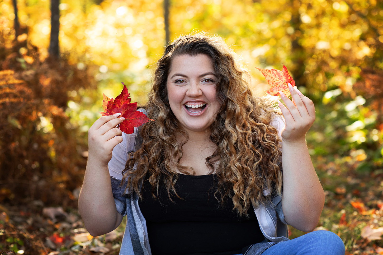 High School Senior Girl laughing holding two fall colored leaves