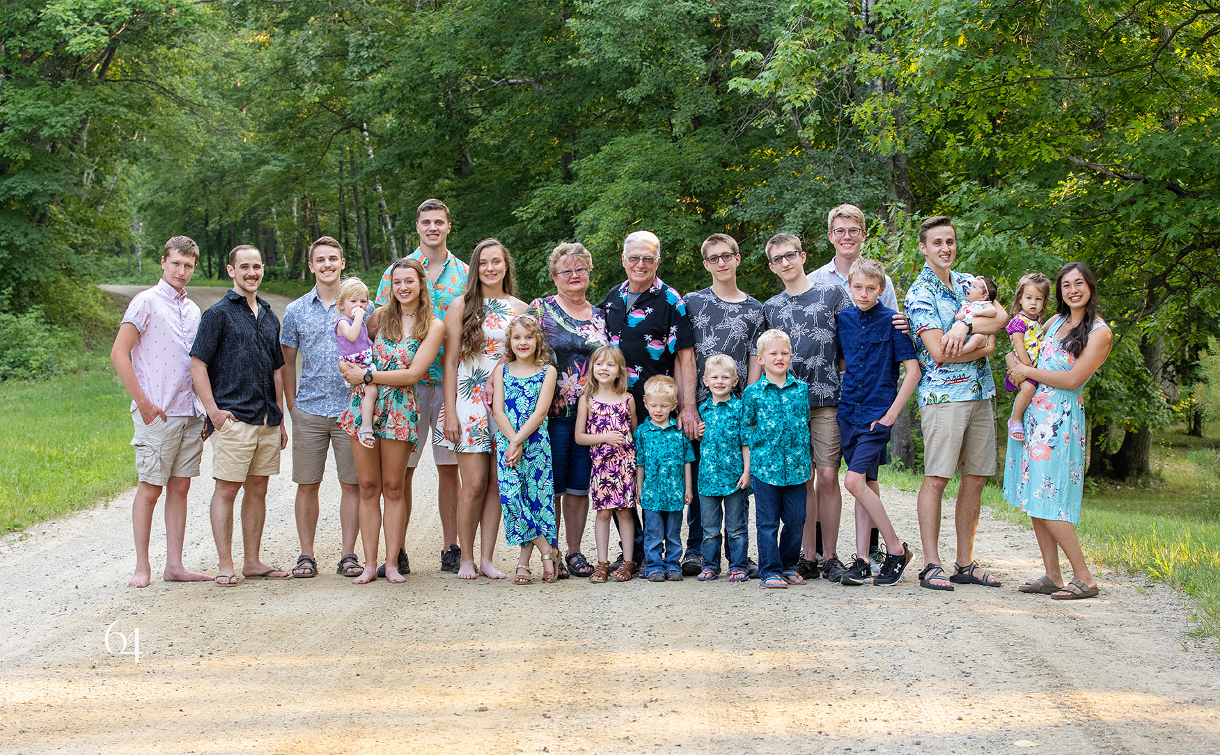 Large group portrait outdoors on a gravel road with grandparents and grandchildren dressed in a hawaiian theme