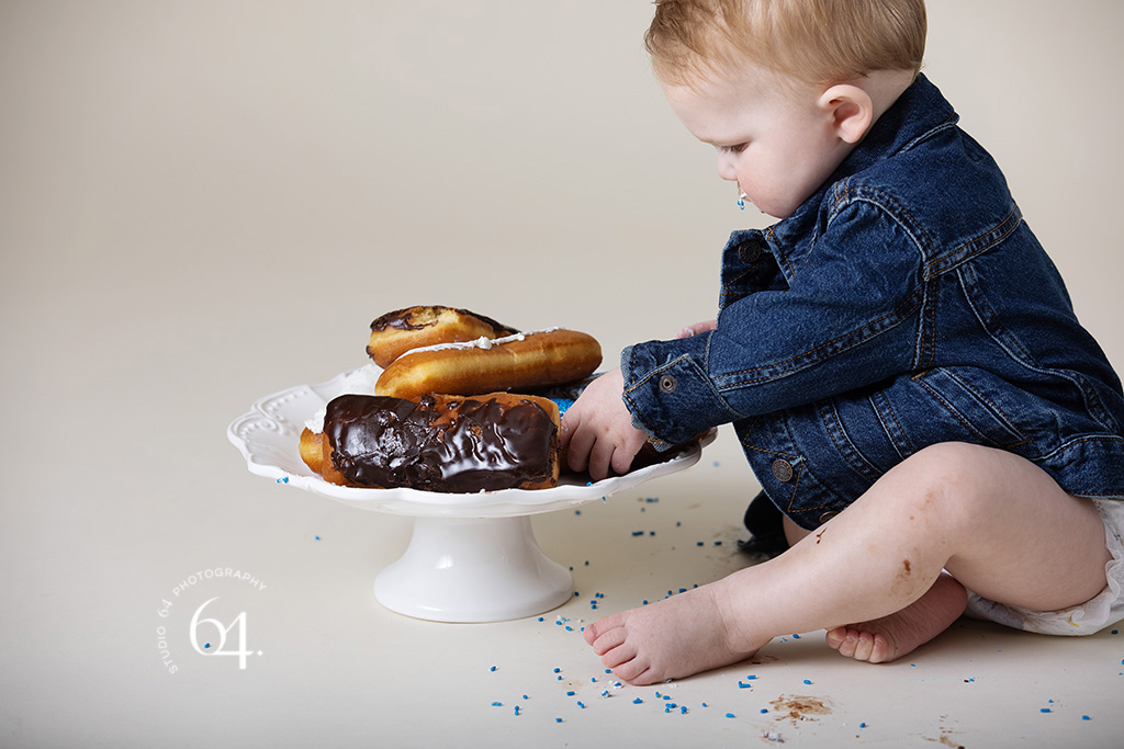 1st year old boy Studio portrait eating a donut wearing a jean jacket and diaper