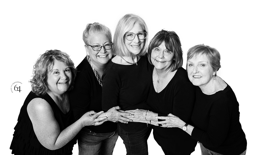 black and white studio image on white backdrop with a group of older women friends embracing